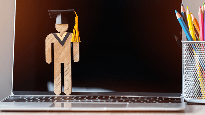 cut out of graduate wearing cap standing on laptop