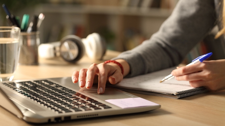 Person writing on a notepad whilst using a laptop