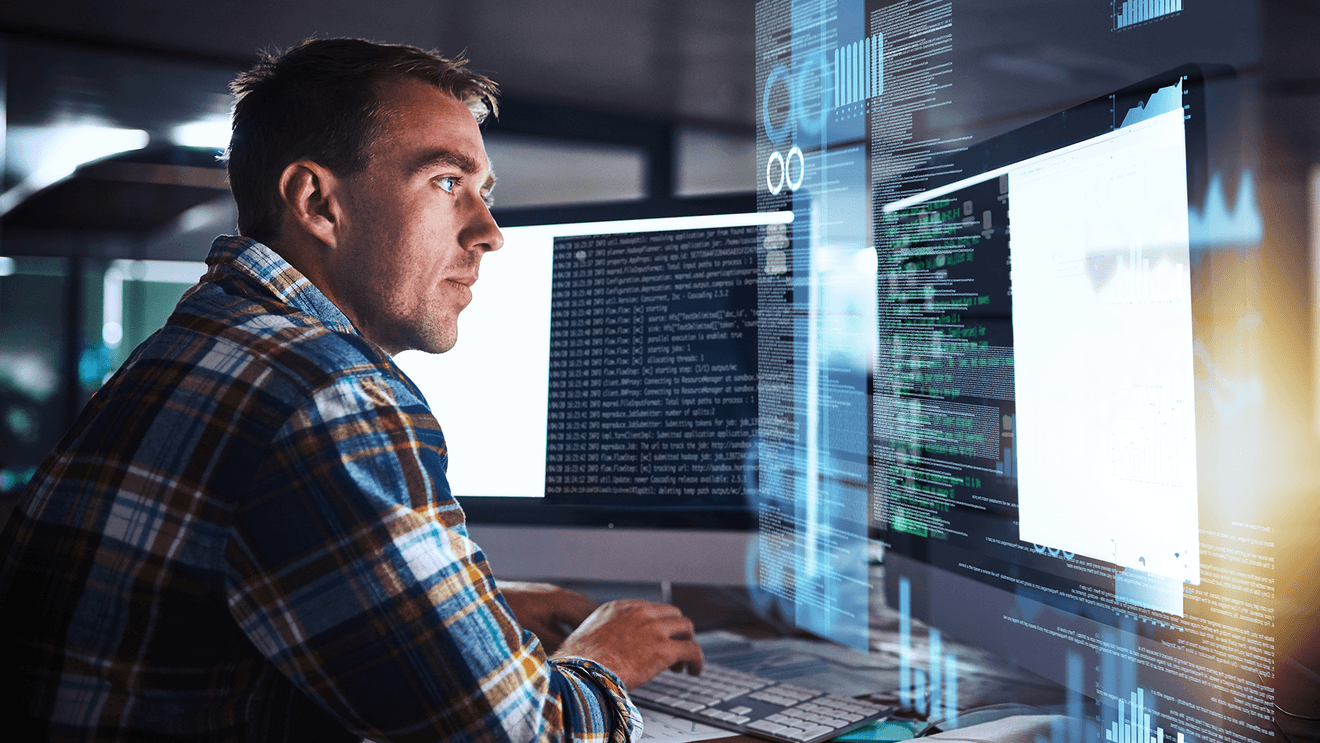 man in flannel typing at desk in front of monitor